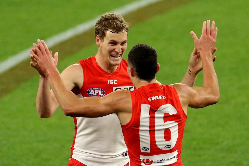 Two Sydney Swans AFL players high-five each other as they celebrate a goal against the GWS Giants.