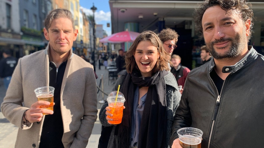 Two men and a woman hold their drinks and smile.