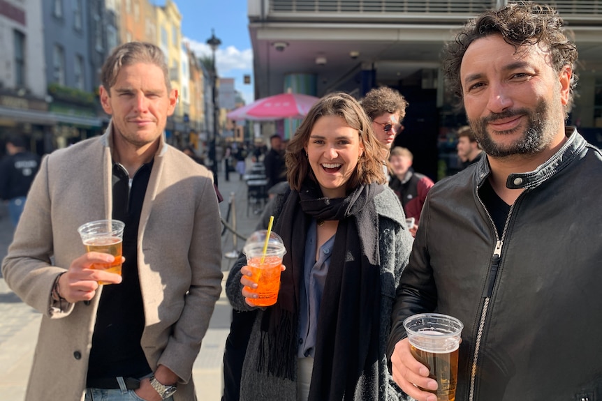 Two men and a woman hold their drinks and smile.