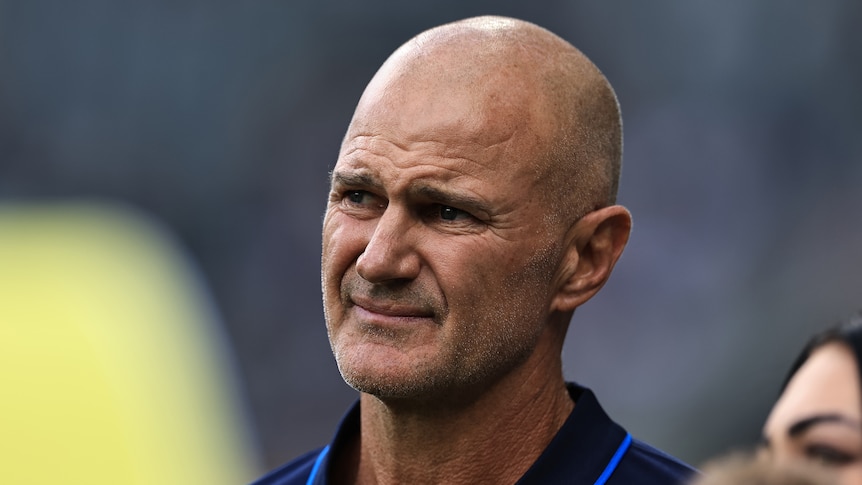 An NRL team coach looks on and grimaces before a match.