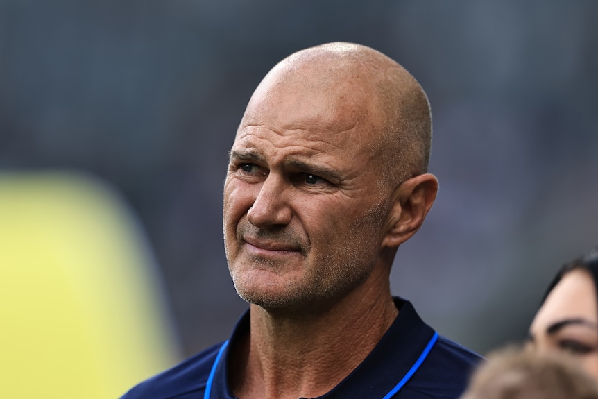 An NRL team coach looks on and grimaces before a match.