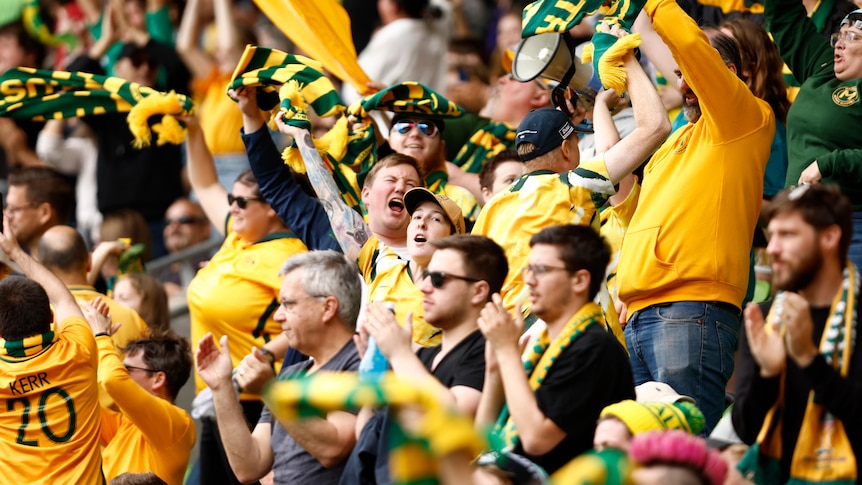 A crowd wearing yellow and green shouts and waves scarves after an exciting moment in a sports game
