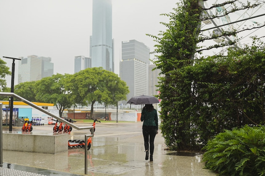 A person with an umbrella walks alone on wet concrete with a misty city in background.