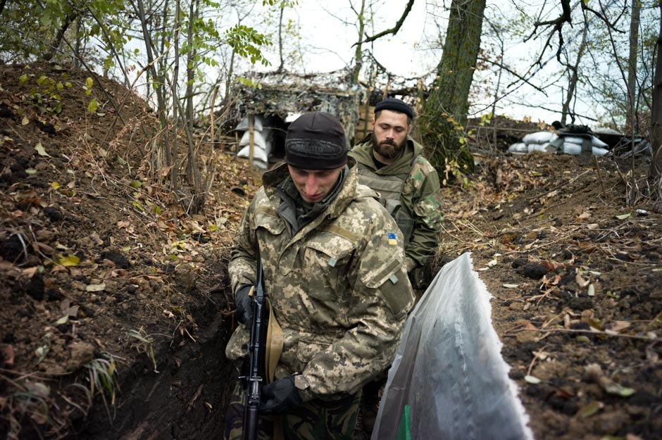 Maxim and a comrade move through the defensive trenches linking the wood and sandbag bunkers that make up their camp.