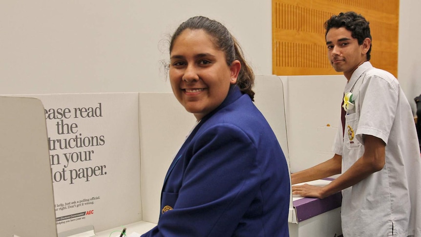 Two Indigenous students in school uniform stand at ballot boxes
