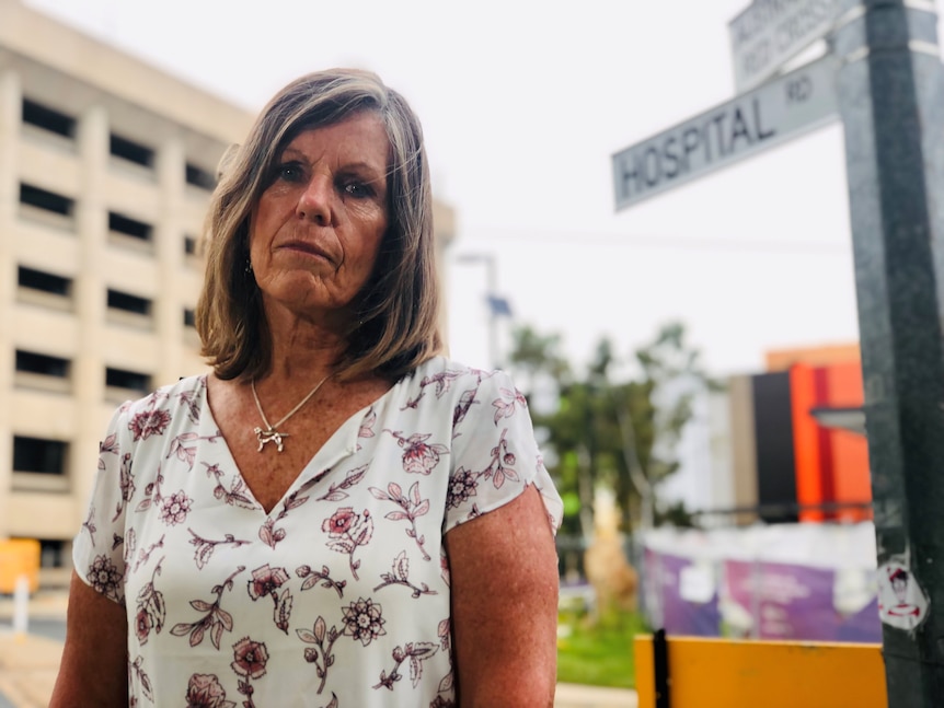 A woman stands in front of a street sign which says "Hospital Road".