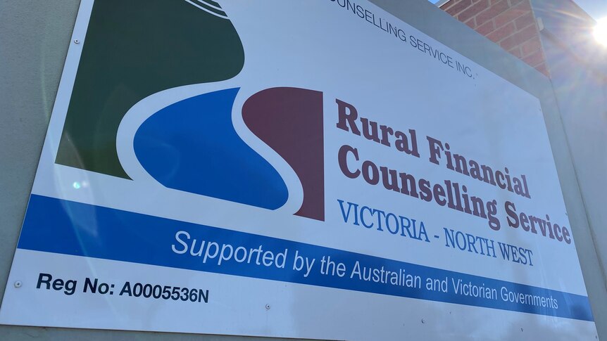 A sign saying Rural Financial Counselling Service on a slight angle with sun peaking through over the building.