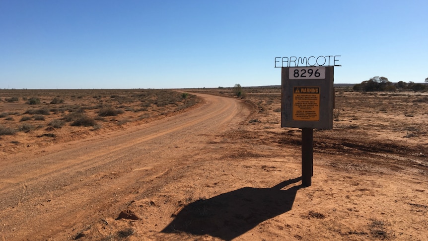 A dirt road winds past a sign for Farmcote station, surrounded by dry red earth with not a cloud in the sky.