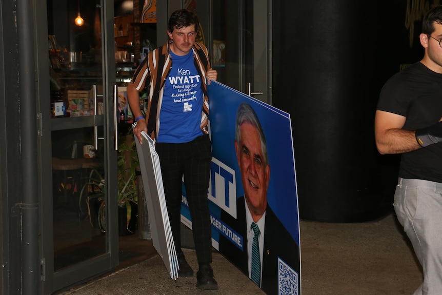 A volunteer removes a Ken Wyatt sign