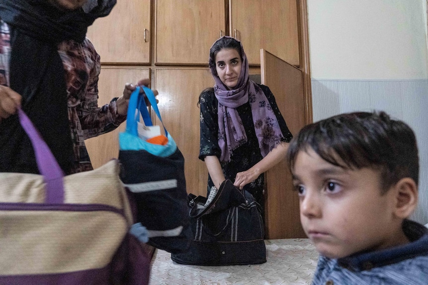 A woman in a purple headscarf stuffs belongings into a bag.