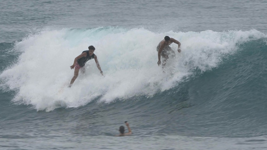 Two Islander men riding a wave together 