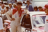 A man in overalls leans on a car with Brock written on it.