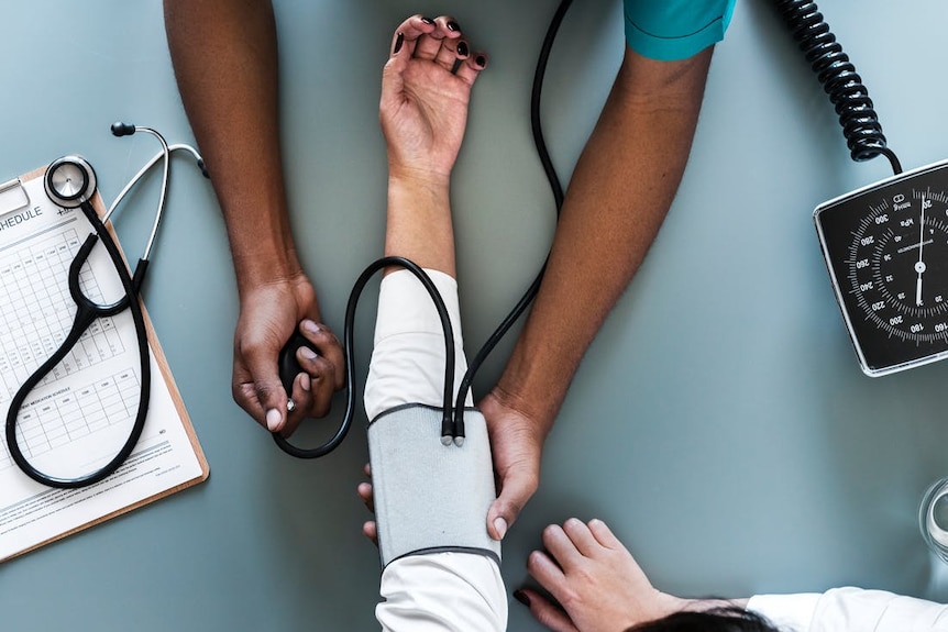 tightly cropped image, you can see a doctors hands giving a blood pressure test to someone with painted nails.