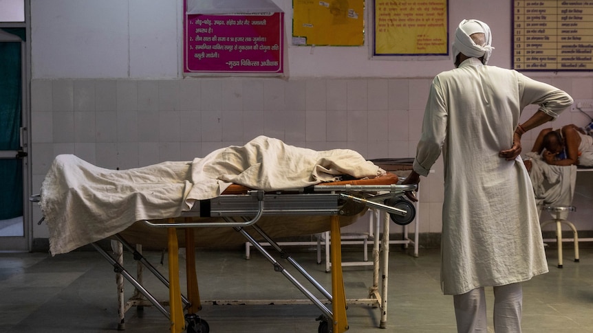 An Indian COVID-19 patient lies on a hospital bed with a man in white standing next to him