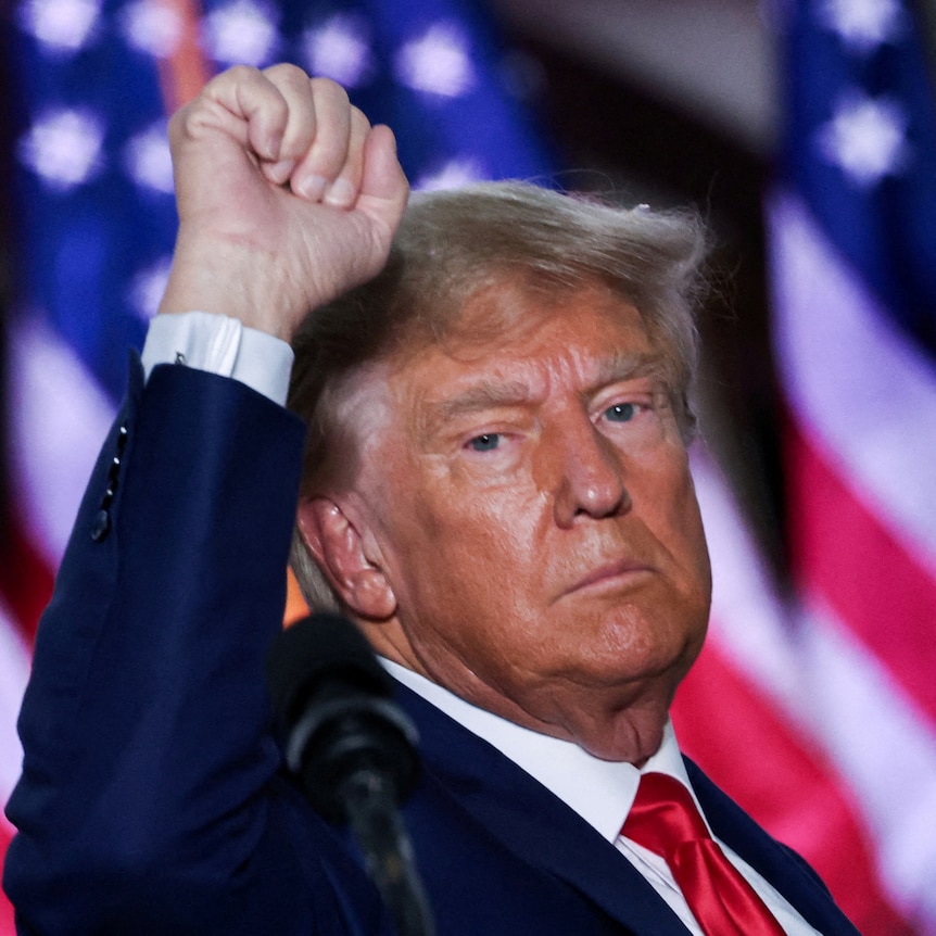 Trump in front of a US flag, raising his fist 