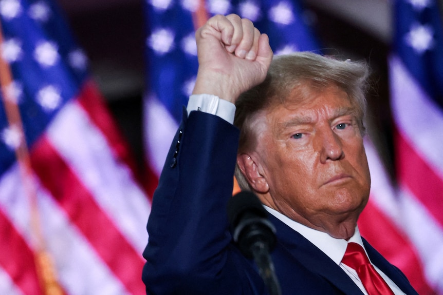 Trump in front of a US flag, raising his fist 