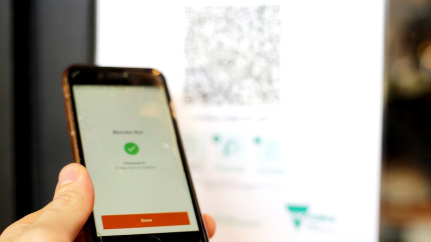 A hand holds a mobile phone with the orange Service Victoria app open to sign in with a QR code.