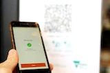 A hand holds a mobile phone with the orange Service Victoria app open to sign in with a QR code.