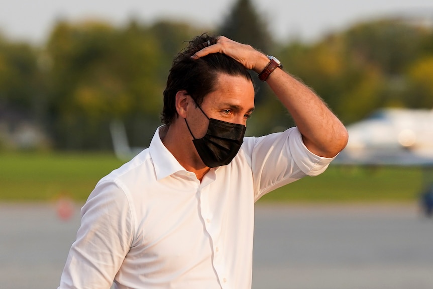 Justin Trudeau in a black face mask pushes his hair back 