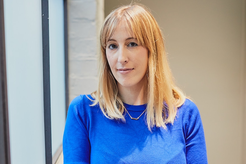 A woman in a blue jumper poses for the camera. 