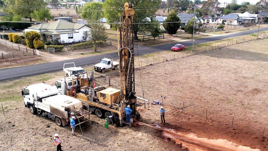 Men work around a large drill attached to the back of a truck parked on grass.