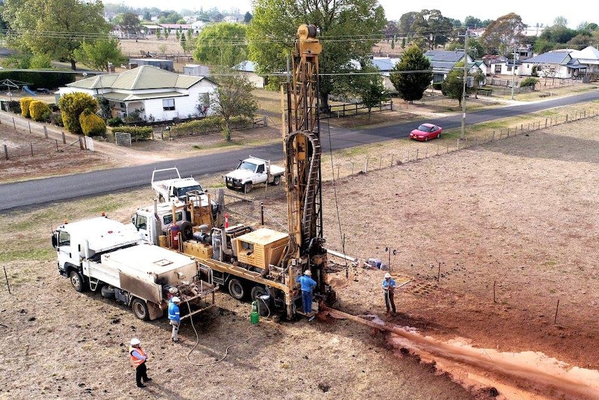 Men work around a large drill attached to the back of a truck parked on grass.