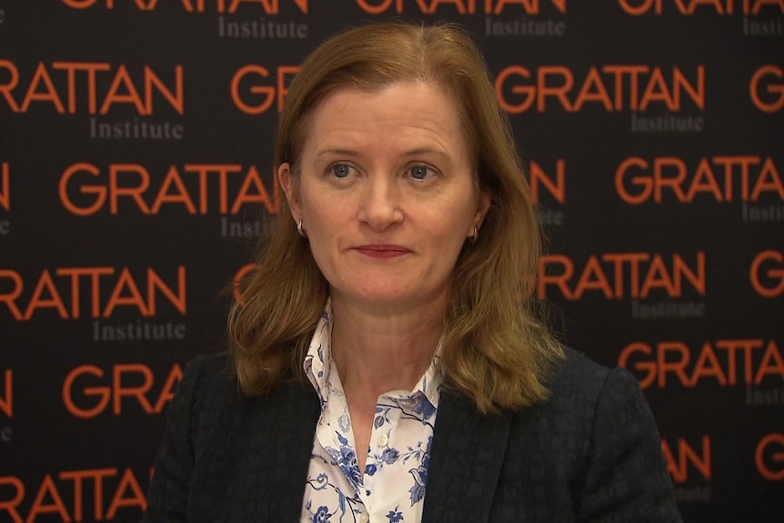 A woman stands in front of wallpaper which says "Grattan Institute"