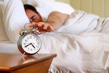 A man reaching out for an alarm clock while still in bed.