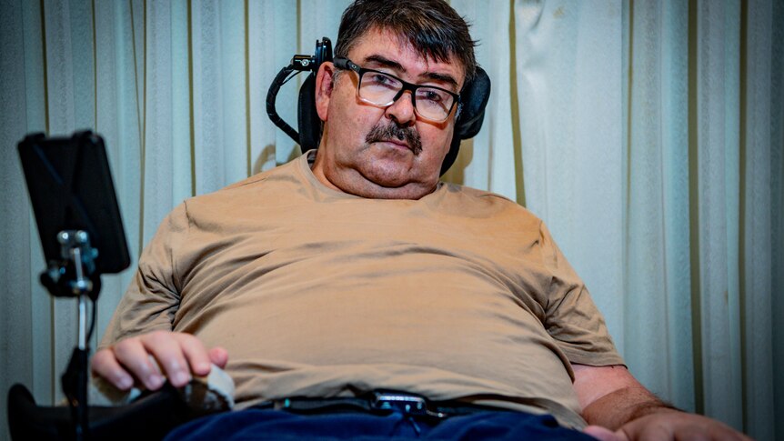 Mark Butler sitting back in a motorised wheelchair, looking pensive.
