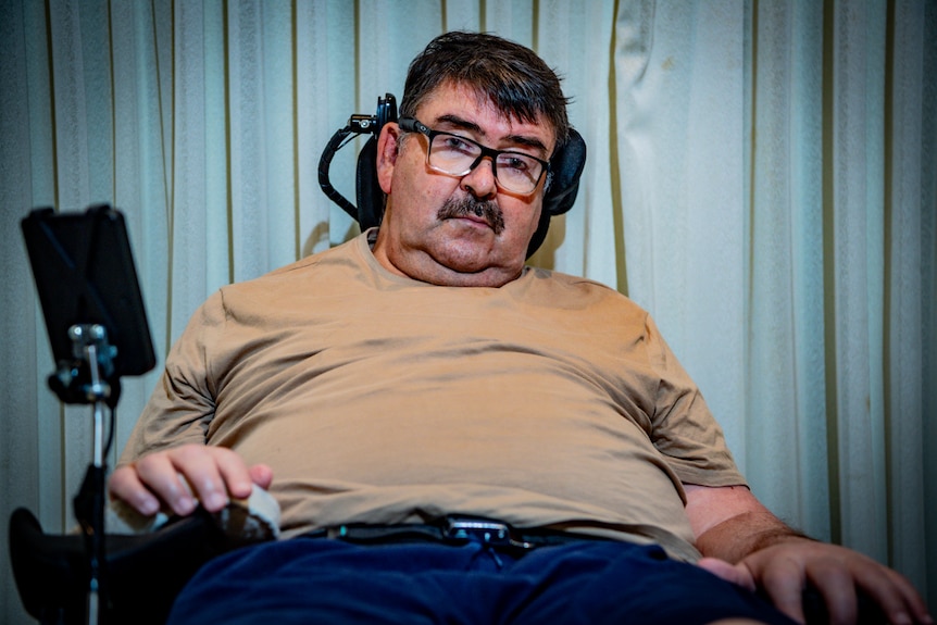 Mark Butler sitting back in a motorised wheelchair, looking pensive.