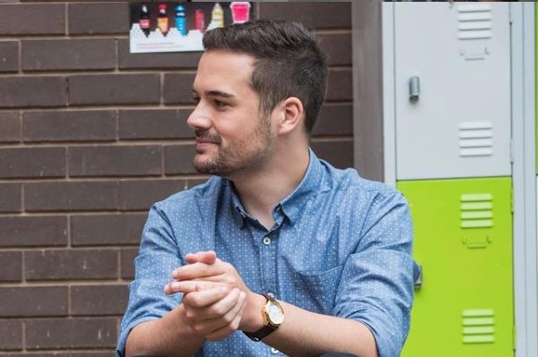 A man sitting next to a school locker outside looking to his left.