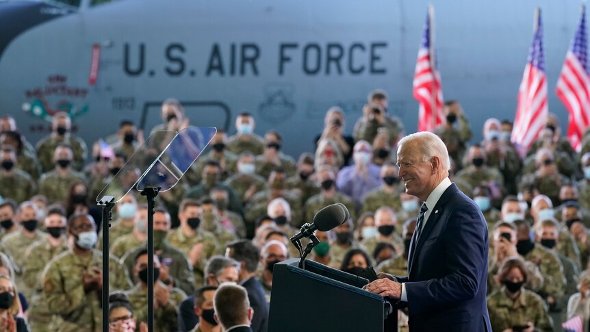 US President Joe Biden speaks in front of a crowd of soldiers as the presidental plane is seen behind them.