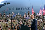 US President Joe Biden speaks in front of a crowd of soldiers as the presidental plane is seen behind them.