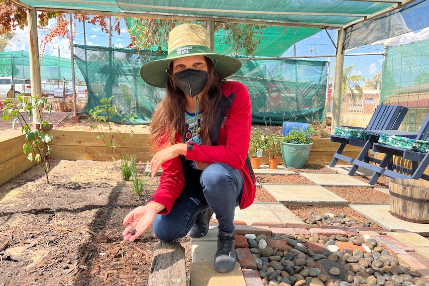 A woman crouches down inside a greenhouse.