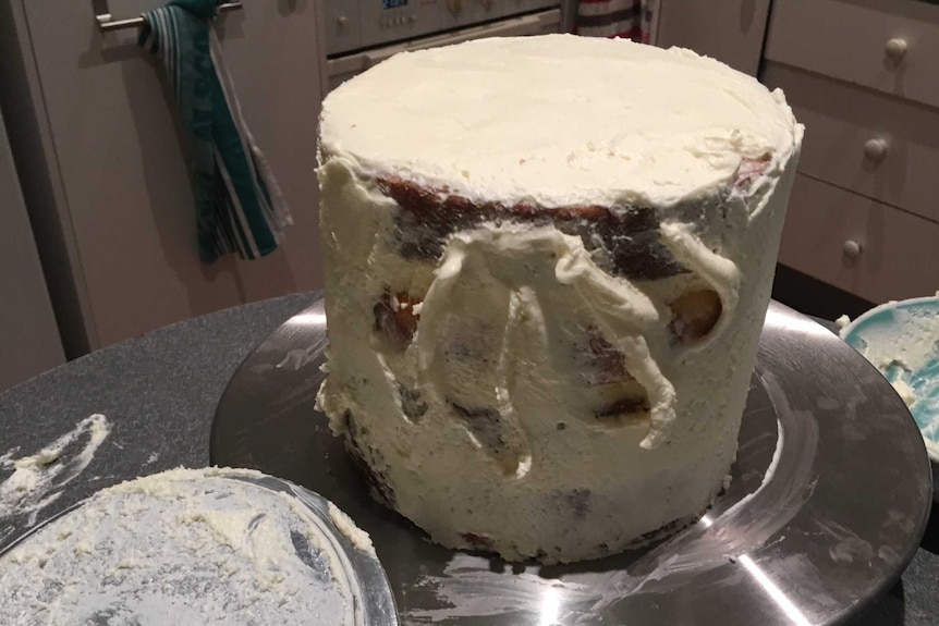 The top tier of a wedding cake in a kitchen, with a handprint on the icing after it was dropped and caught.