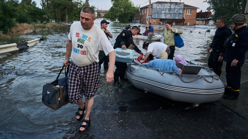 A man carries a bag as others behind him get into inflatable rafts as waters rise. 