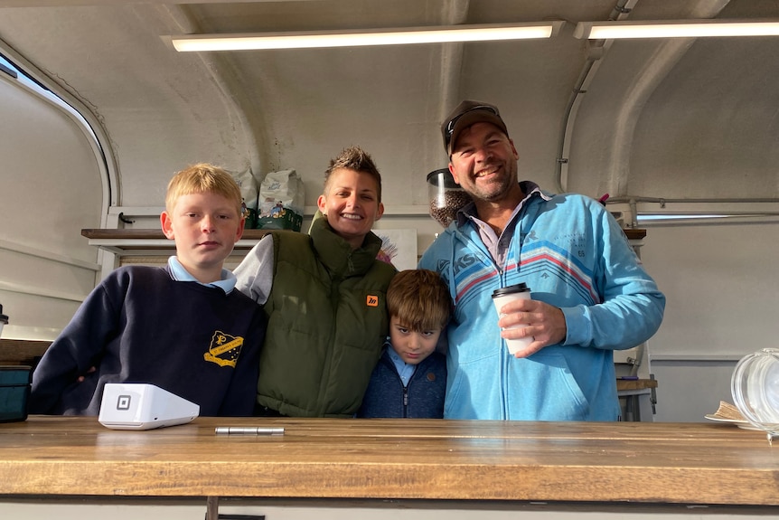 A mum, dad and two young boys stand behind the counter in a food truck, smiling.