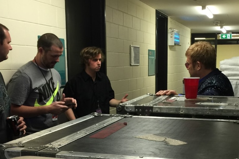 A group of men talking in a corridor backstage at a stadium.