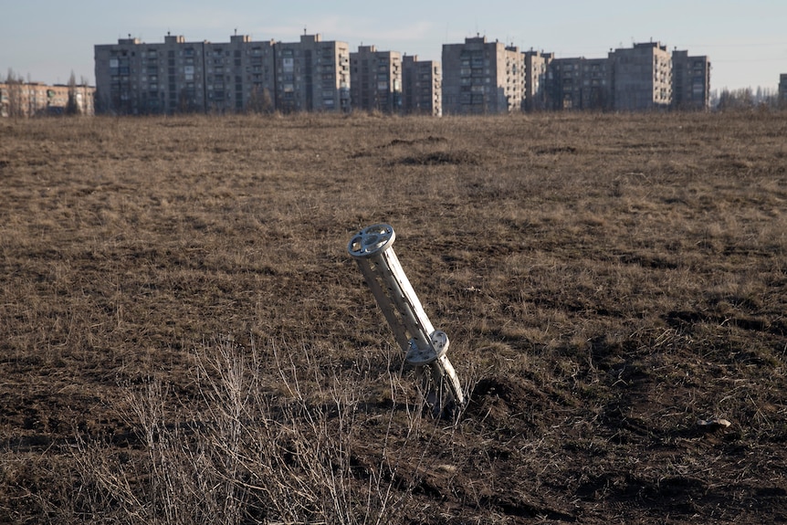 An emptied cluster munitions container is seen stuck in the ground outside apartment blocks.