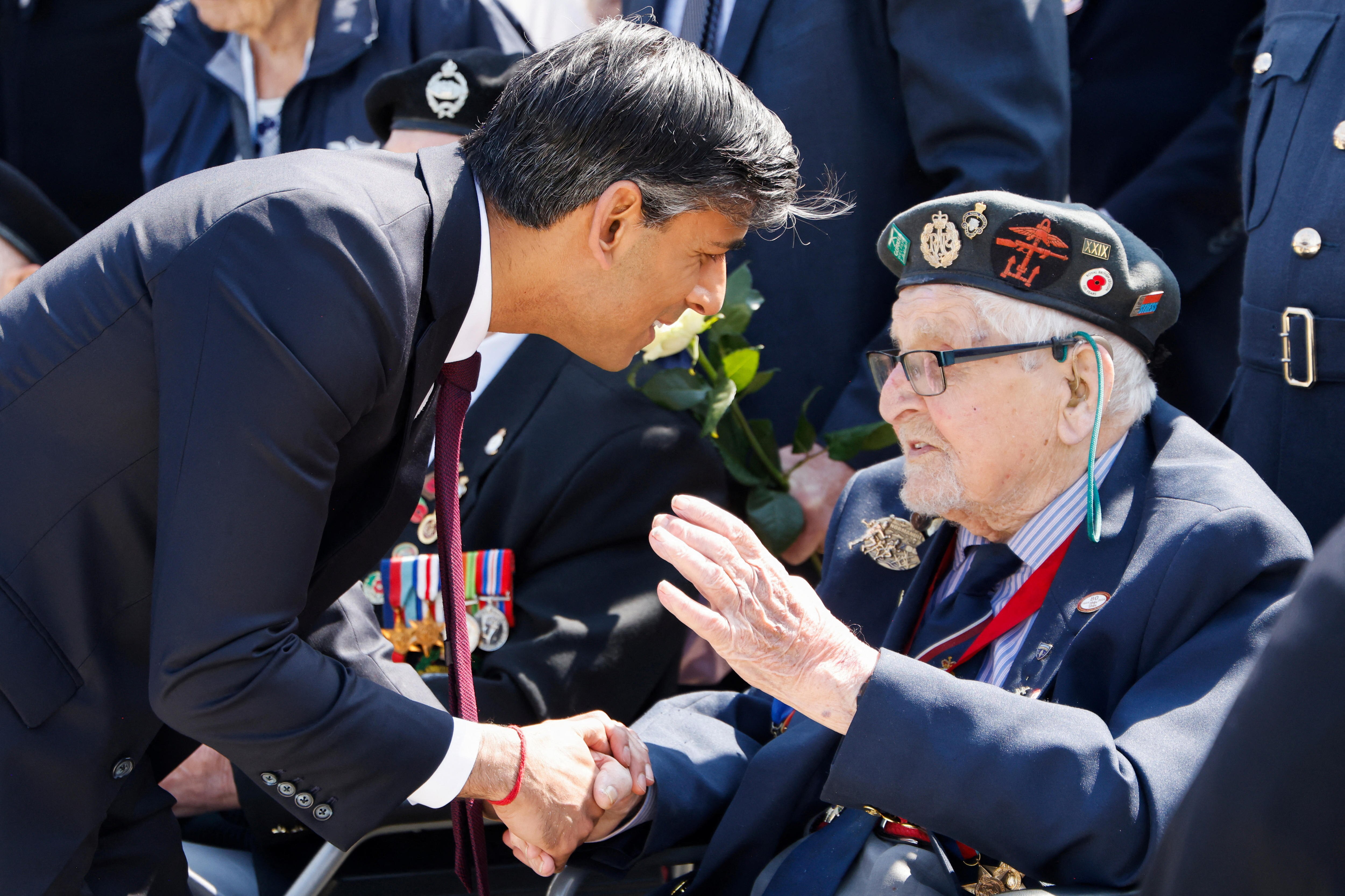  A man crouches down to shake the hand of an older man sitting down.
