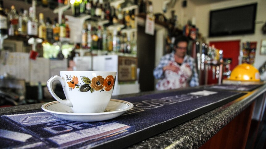 A painted teacup sits on a country pub's bar, with a beer mat under it.