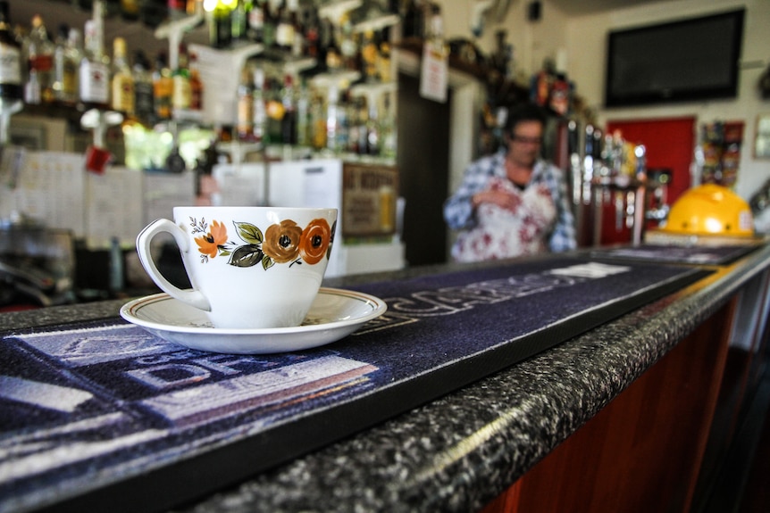 A painted teacup sits on a country pub's bar, with a beer mat under it.