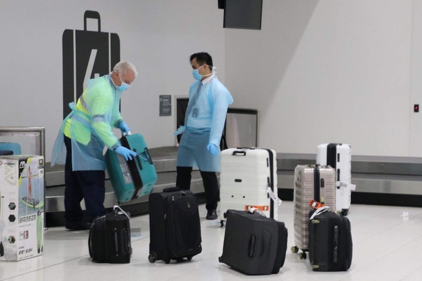 Baggage handlers at Perth Airport remove suitcases from the carousel, while wearing protective gear, including gloves and masks.