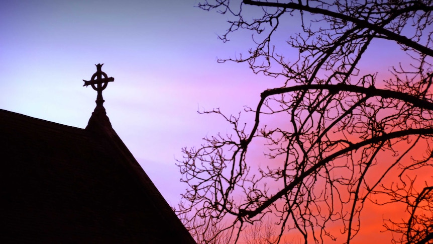Cross atop a church or chapel within a university campus, at sunset.