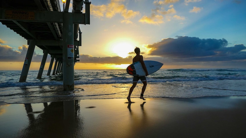 Surfer silhouetted against sunrise at the beach