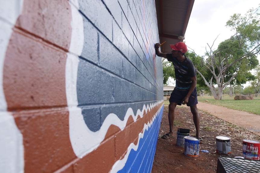A man paints a mural on the side of a brick wall
