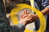 Two people holding hands with a yellow brush stroke around their hands to depict how to help lonely people over Christmas.