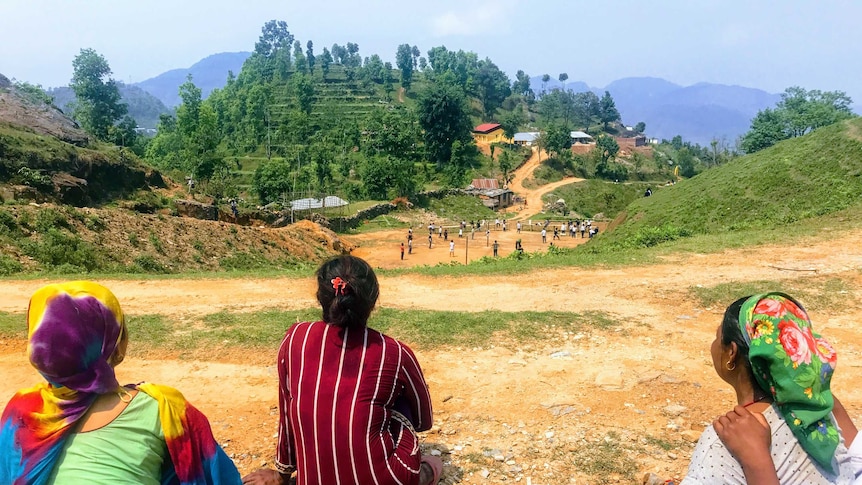 Three women overlook a number of children playing at a school on the hillside.