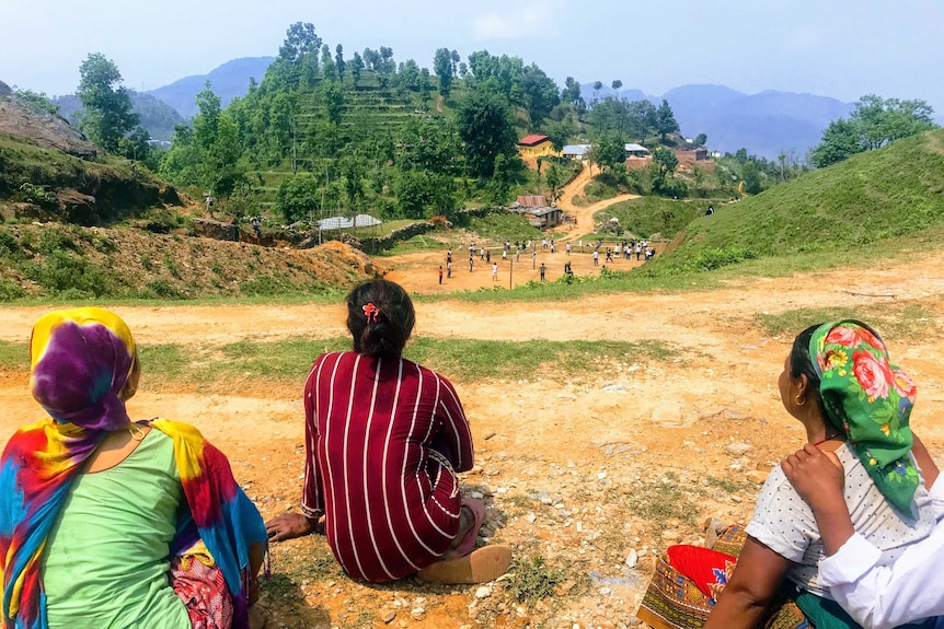 Three women overlook a number of children playing at a school on the hillside.