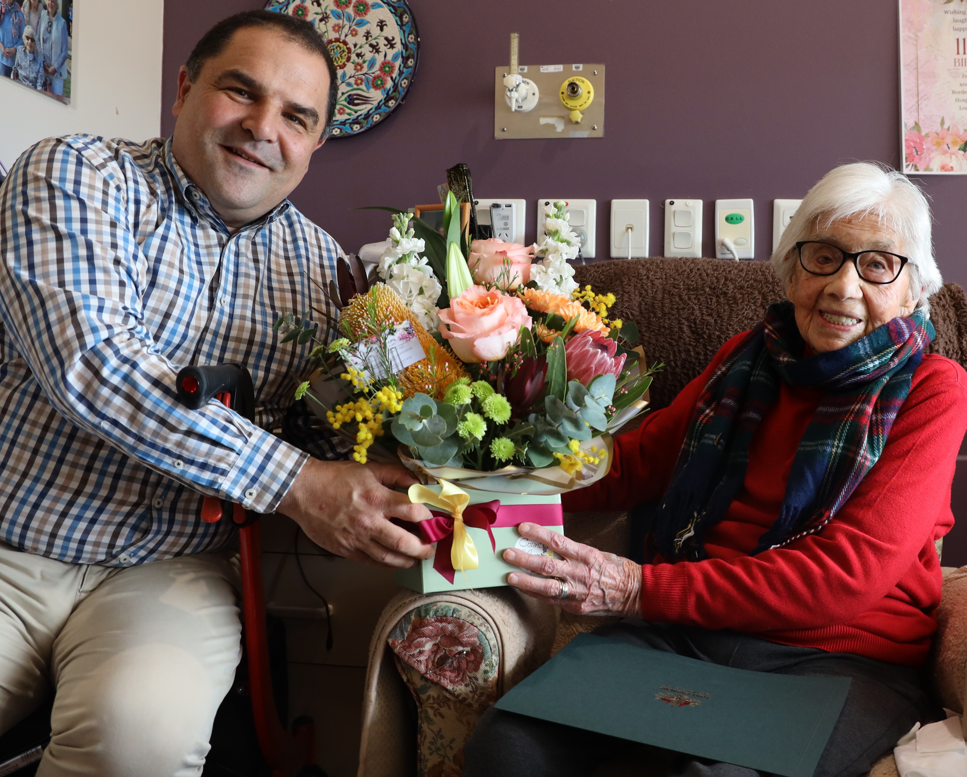 A man presents an elderly lady with flowers and a certificate on her 112th birthday 